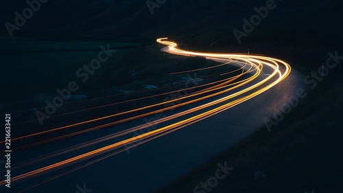 Car light trails moving fast on a dark winding road at night