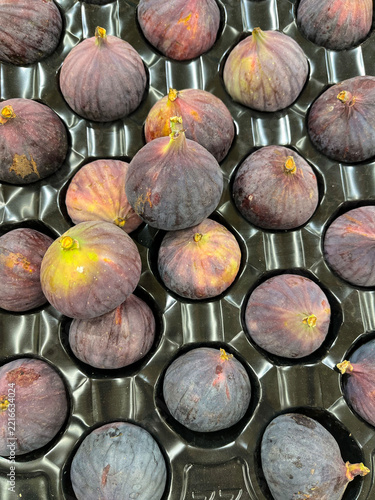 Fresh purple fig fruits in the cells of a black plastic tray.