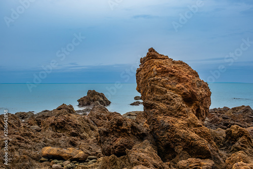 Rugged coastal rocks meet a calm deep-blue sea beneath a clear sky; textured stone formations and tranquil waters create an elegant, minimalist wallpaper.