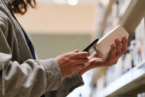 A shopper is examining a product while using a smartphone to scan its barcode, showcasing the integration of technology in retail shopping experiences.