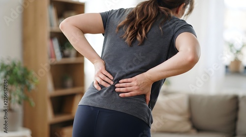 Woman suffering from lower back pain standing in a living room at