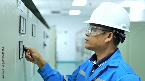 Electrical engineer inspecting a control panel and industrial power system inside a modern electrical control room in a factory.