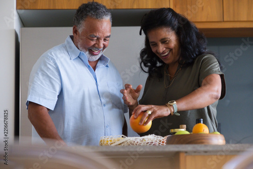 African American couple standing at kitchen counter handling orange with reusable mesh bag