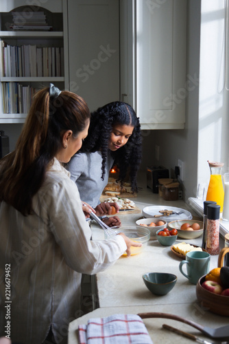 African American mother and daughter in sweater, striped shirt preparing meal at counter with eggs