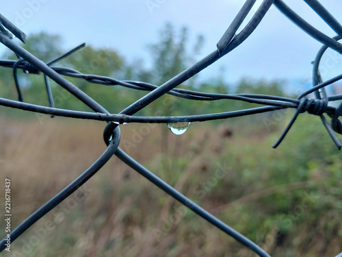 Single Water Drop Hanging on Wire Fence with Reflected Landscape Close Up