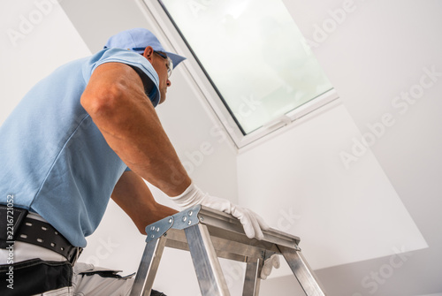 Worker inspecting a roof window from a stepladder