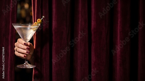 Hand holding a martini glass with olives behind dark red velvet