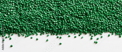 Vibrant emerald green plastic pellets create a dense textured surface, scattering onto a clean white background, symbolizing industrial raw materials, sustainable manufacturing, and