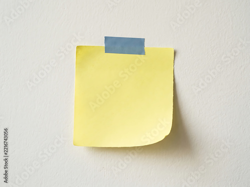 Yellow sticky note attached to a wall with blue tape