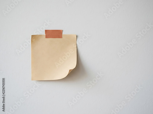 Beige sticky note taped to a wall with masking tape