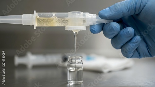 Medical Professional Filling Clear Liquid into Small Glass Vial with Syringe