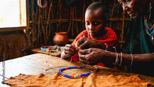 Maasai grandmother and grandson making traditional beaded jewelry