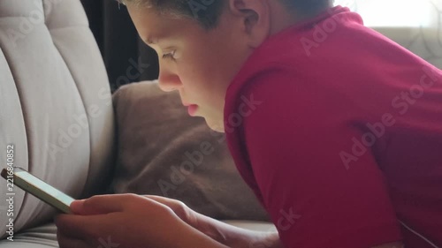 Close-up of a young boy looking at a smartphone screen. Focused expression, profile view, sitting on a sofa at home, screen light, technology.