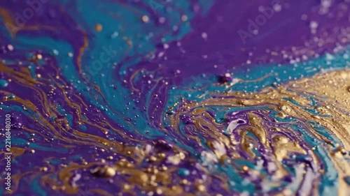 Close-up of swirling gold and purple marbled paint in motion