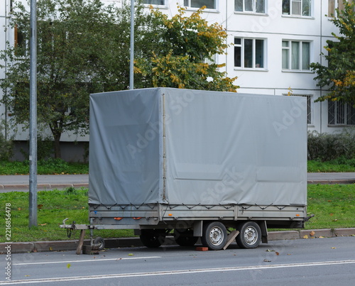 A tall four‑wheeled awning car trailer stands on the road near the lawn