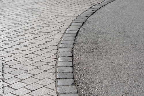 Curved asphalt road edge bordering a cobblestone pavement