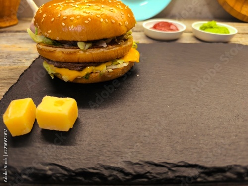A gourmet grilled burger with fresh tomato slices and aromatic rosemary, served on sesame seed buns on a cutting board