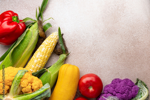 Fresh vegetables including corn and peppers arranged on a light stone background with copy space