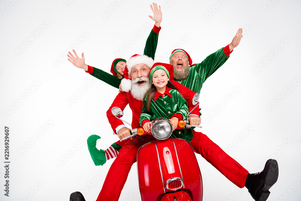 Fototapeta premium Santa and two elves riding a red scooter with a smiling child, laughing and celebrating Christmas holiday spirit and family fun