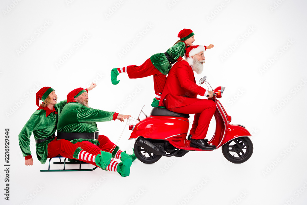 Fototapeta premium Santa and playful elves riding a red scooter and sled for a festive family Christmas holiday full of joy, laughter and seasonal fun