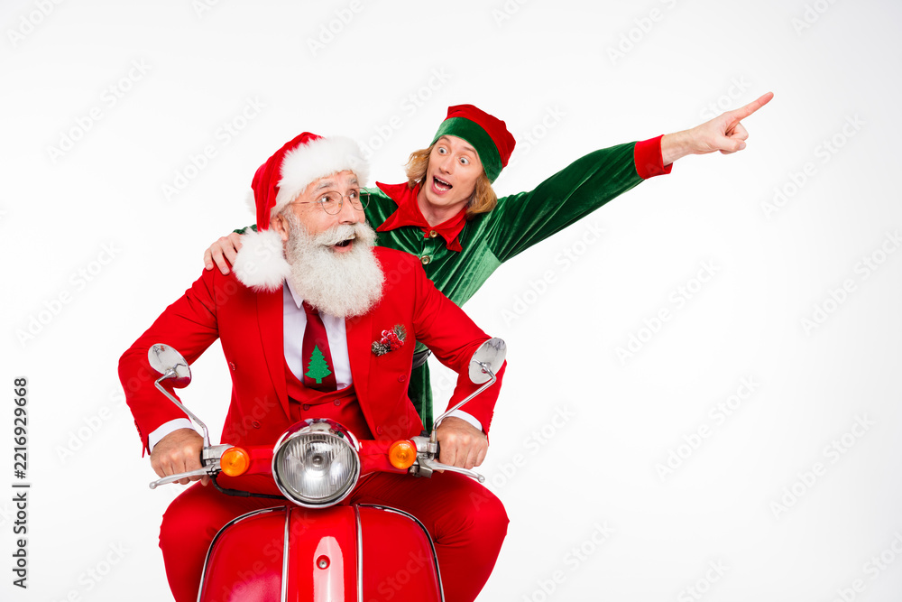 Fototapeta premium Santa Claus and excited elf riding a red scooter celebrating Christmas with festive outfits and joyful expressions