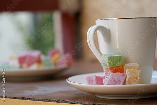 A close-up view of traditional, colorful Turkish delight cubes served with a white Turkish coffee cup.
