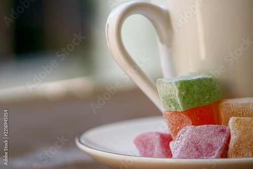 A close-up view of traditional, colorful Turkish delight cubes served with a white Turkish coffee cup.
