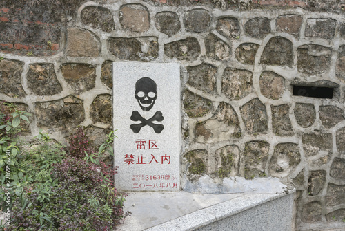Minefield Warning Sign with Skull and Crossbones on Stone Wall in Dongxing, Guangxi