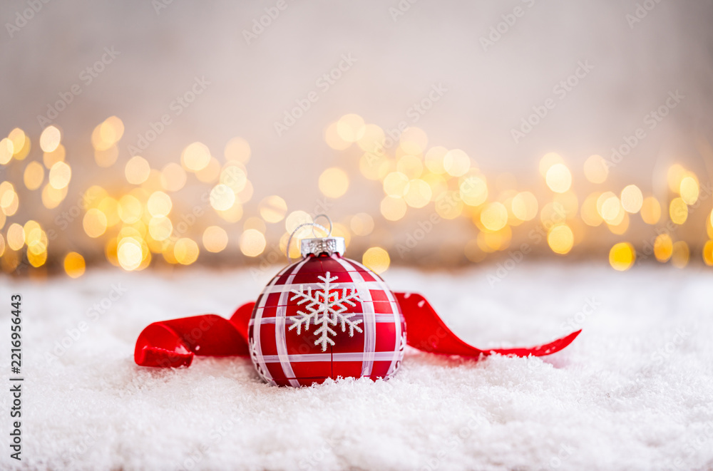 Fototapeta premium A Christmas background featuring red baubles with golden glitter stripes, a star, and ribbon framing wide snowy ground, softly lit by warm twinkling lights with generous copy space.