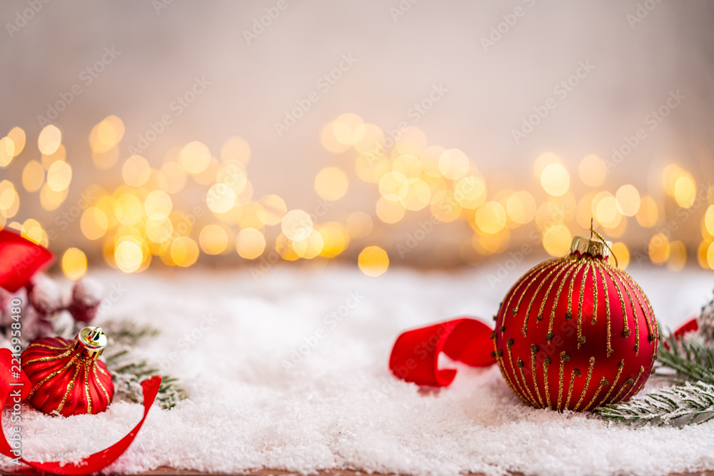 Fototapeta premium A Christmas background featuring red baubles with golden glitter stripes, a star, and ribbon framing wide snowy ground, softly lit by warm twinkling lights with generous copy space.