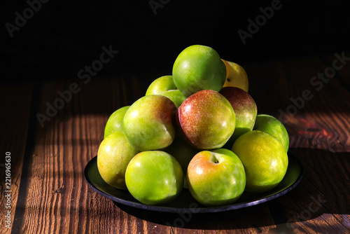 Fresh Green and Red Plums on a Black Plate on Rustic Wooden Table
