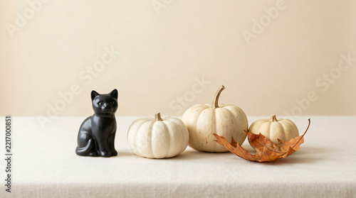 Black cat Halloween joyful autumn still life with Small black cat figurine beside pale pumpkins and a curved autumn leaf for seasonal advertising, with subtle magical glow