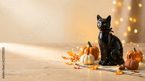Cozy festive composition with Glossy black cat ornament with orange pumpkins and soft golden lights for Halloween promotion, in a polished commercial composition