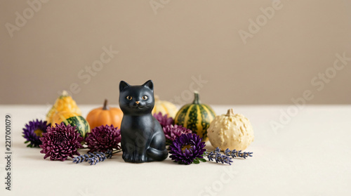 Tiny black cat decoration surrounded by purple flowers and miniature gourds in a soft-spooky seasonal scene for strong seasonal visual impact, with soft studio light