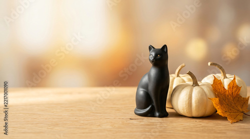 Black cat Halloween magical holiday concept with Small black cat figurine beside pale pumpkins and a curved autumn leaf for seasonal advertising, with soft studio light