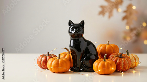 Soft-spooky seasonal scene with Glossy black cat ornament with orange pumpkins and soft golden lights for Halloween promotion, in a colorful seasonal setting