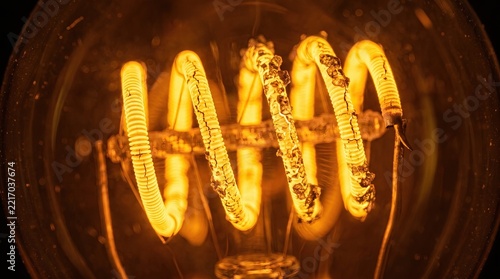 Extreme macro shot of a glowing spiral filament inside a vintage light bulb emitting a warm amber light against a dark background representing innovation and the spark of a creative idea