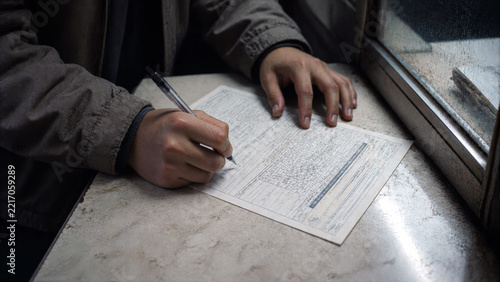 Person filling out a detailed paper form by hand at a service counter, representing applications, registration and administrative paperwork