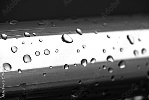 Macro close up of water droplets on a brushed stainless steel metallic surface in monochrome