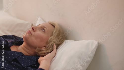 Tired woman in her 50s has headache while lying in bed after poor sleep