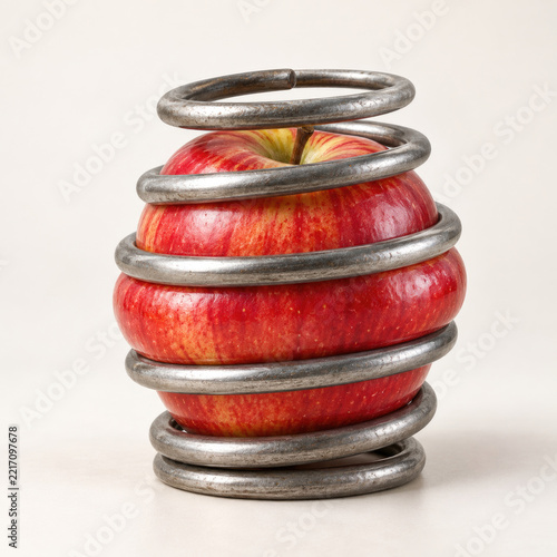 Red apple is compressed inside a thick metal spring.