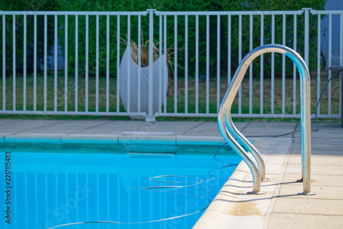 Outdoor swimming pool with metal handrail and safety fence in sunny day