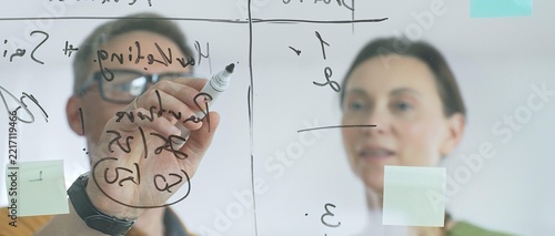 Business professionals reviewing marketing data, sales metrics, and partnership insights on transparent board, collaborating with sticky notes in modern workplace setting