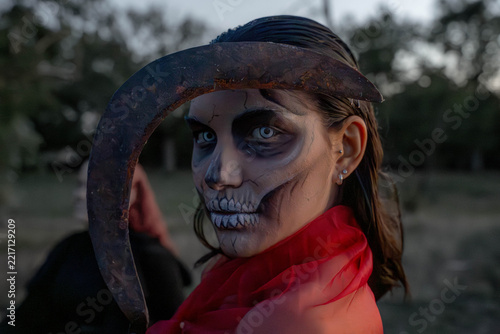 Close-up portrait of person with skull face paint, white contact lenses, rusty sickle prop