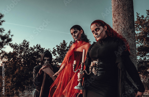 Three costumed figures with skull face paint holding pitchfork and scythe