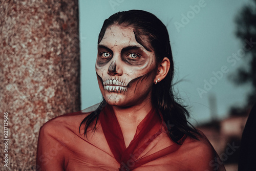 Woman with skull face paint and white contact lenses, red sheer fabric, dramatic Halloween makeup
