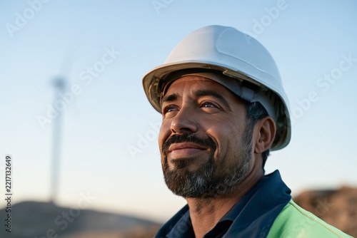 Smiling wind farm engineer in white hard hat outdoors