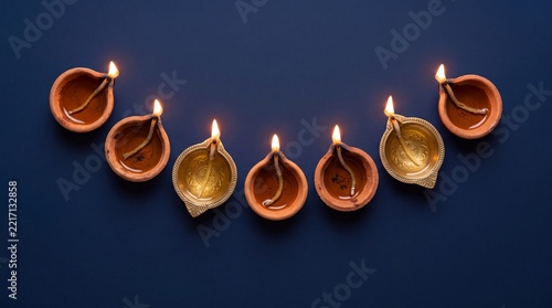 Top view of lit clay and brass Diwali diyas arranged in a curved line on dark navy blue background with copy space