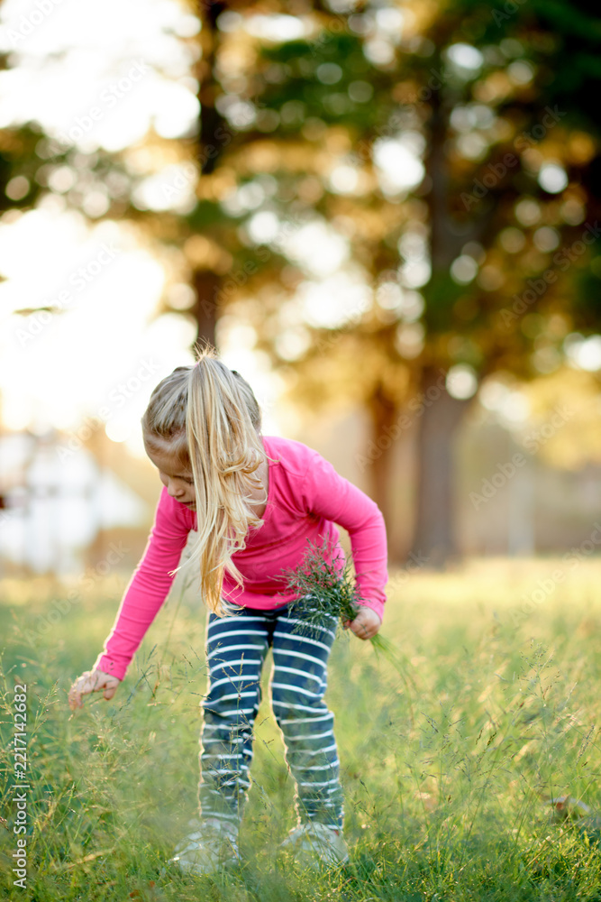 Naklejka premium Park, child and picking grass for play, explore and development in environment with bokeh. Outdoor, girl and kid gathering plants with lawn in nature for collection, learning and growth in spring