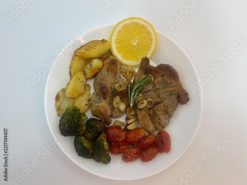 Fotografie Steak with Potatoes, Broccoli, Tomatoes and Lemon on a White Plate, Top View